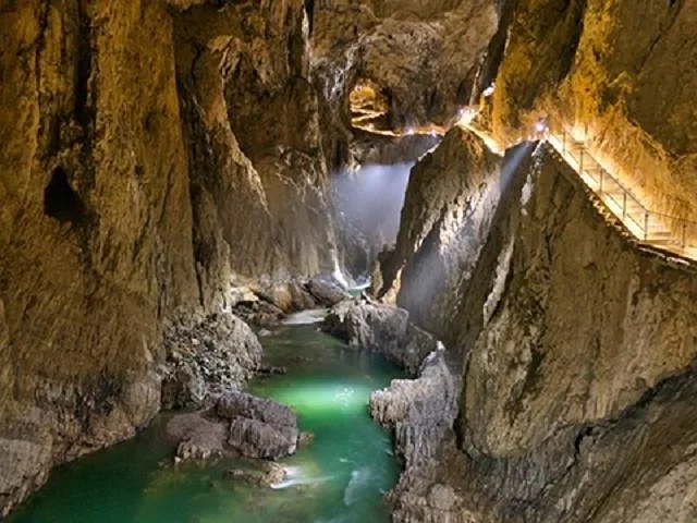 Underground river flowing through a massive cave with a lighted path